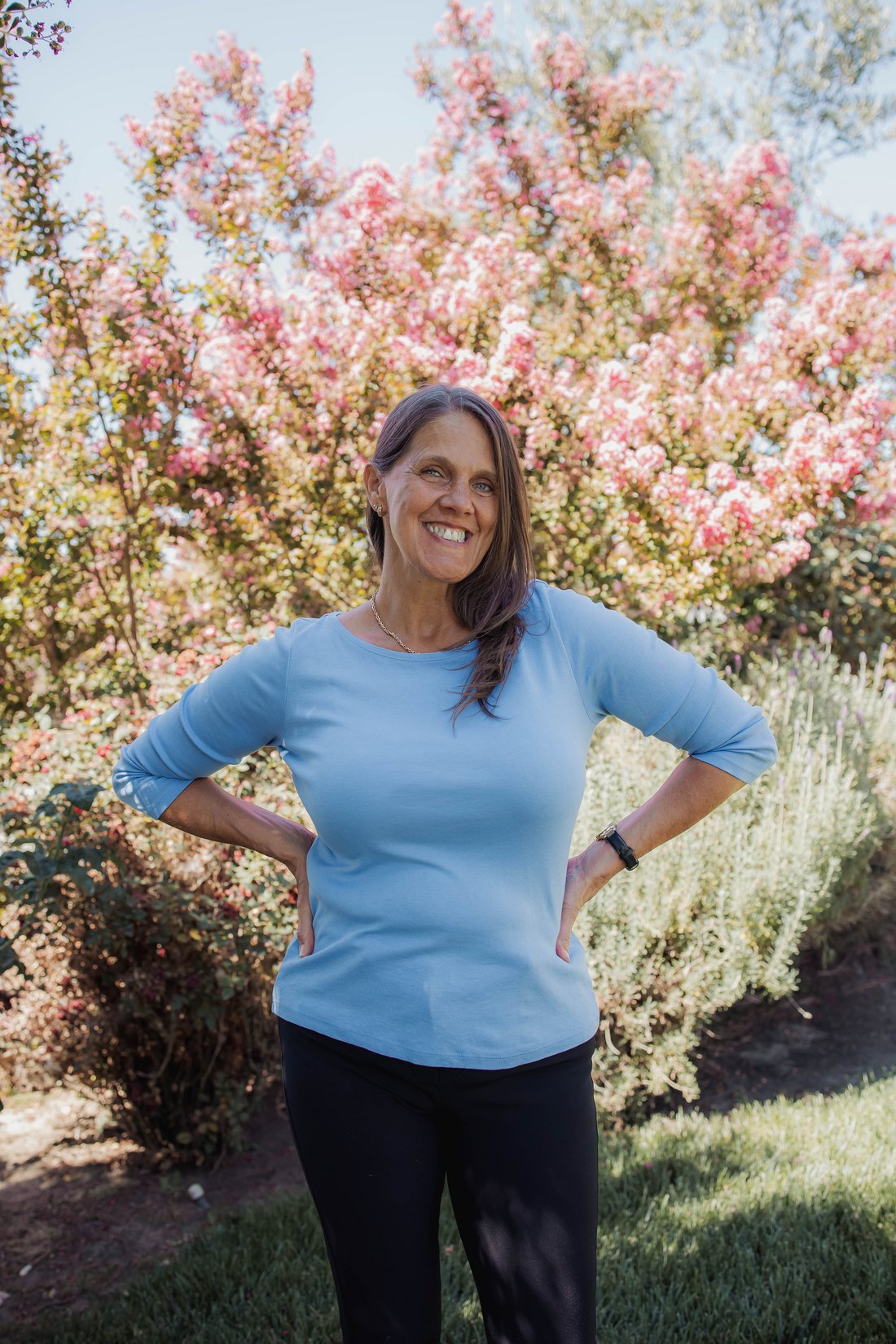 Carrie DeGrandmont outdoors in a light blue top, smiling among pink flowering trees
